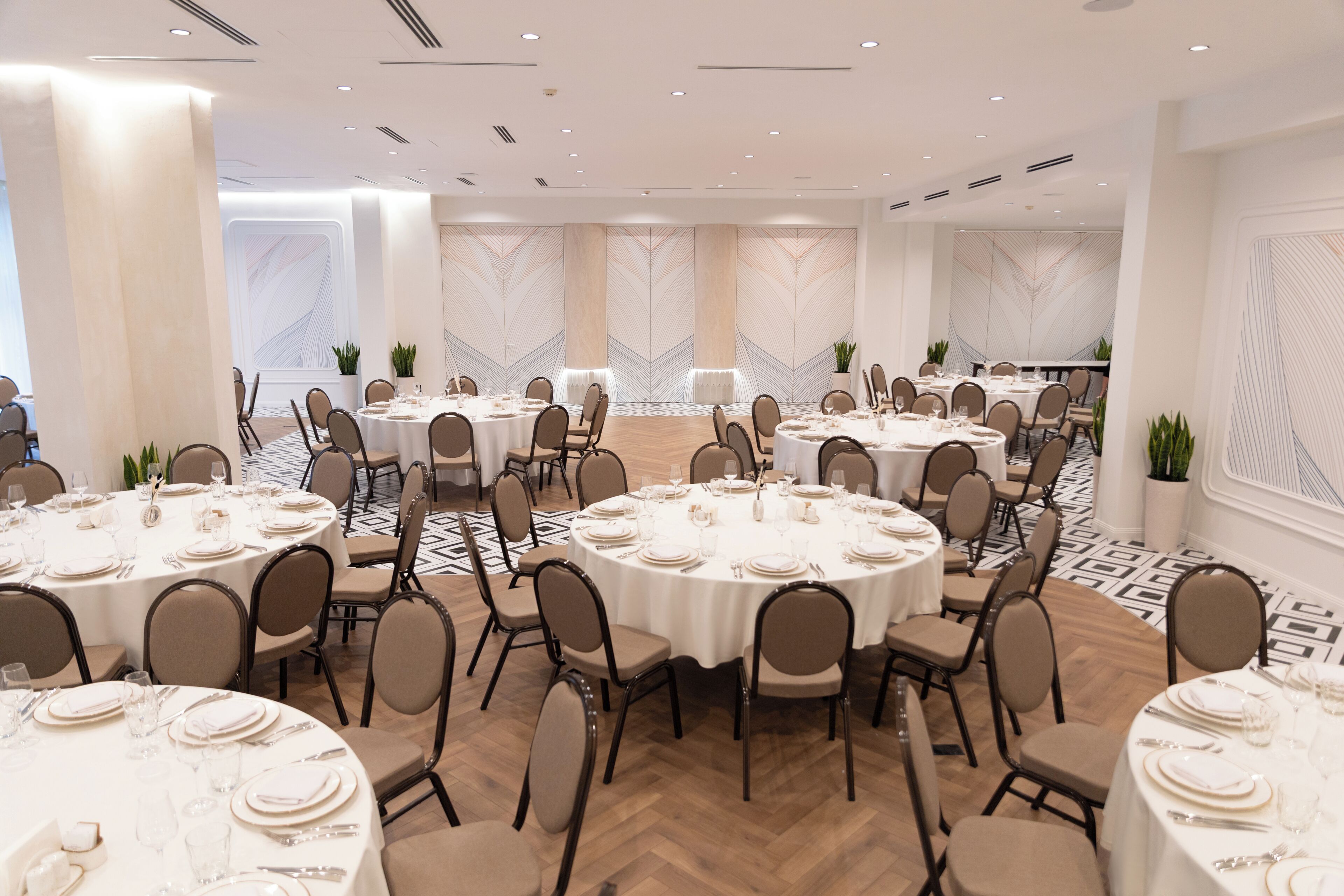 A large conference room with multiple round tables, each set with white tablecloths, plates, and cutlery.