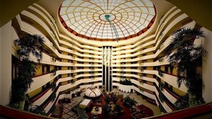 A multi-level atrium with a central glass dome, multiple balconies, and indoor plants. - Rahat Palace Hotel (Almaty)