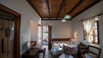A bedroom with a wooden ceiling, a bed with a white duvet, a desk with a computer, a chair, and a window with curtains.