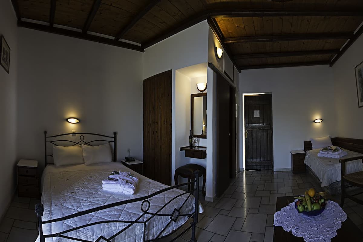 A bedroom with a bed, bedside tables, a desk, a chair, a television, and a fruit bowl.