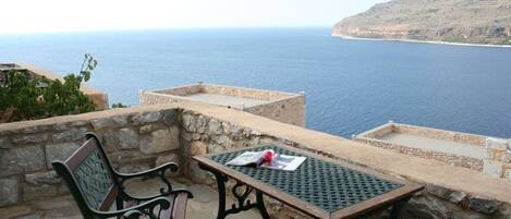 A stone patio with a table and chairs overlooking a coastal view.