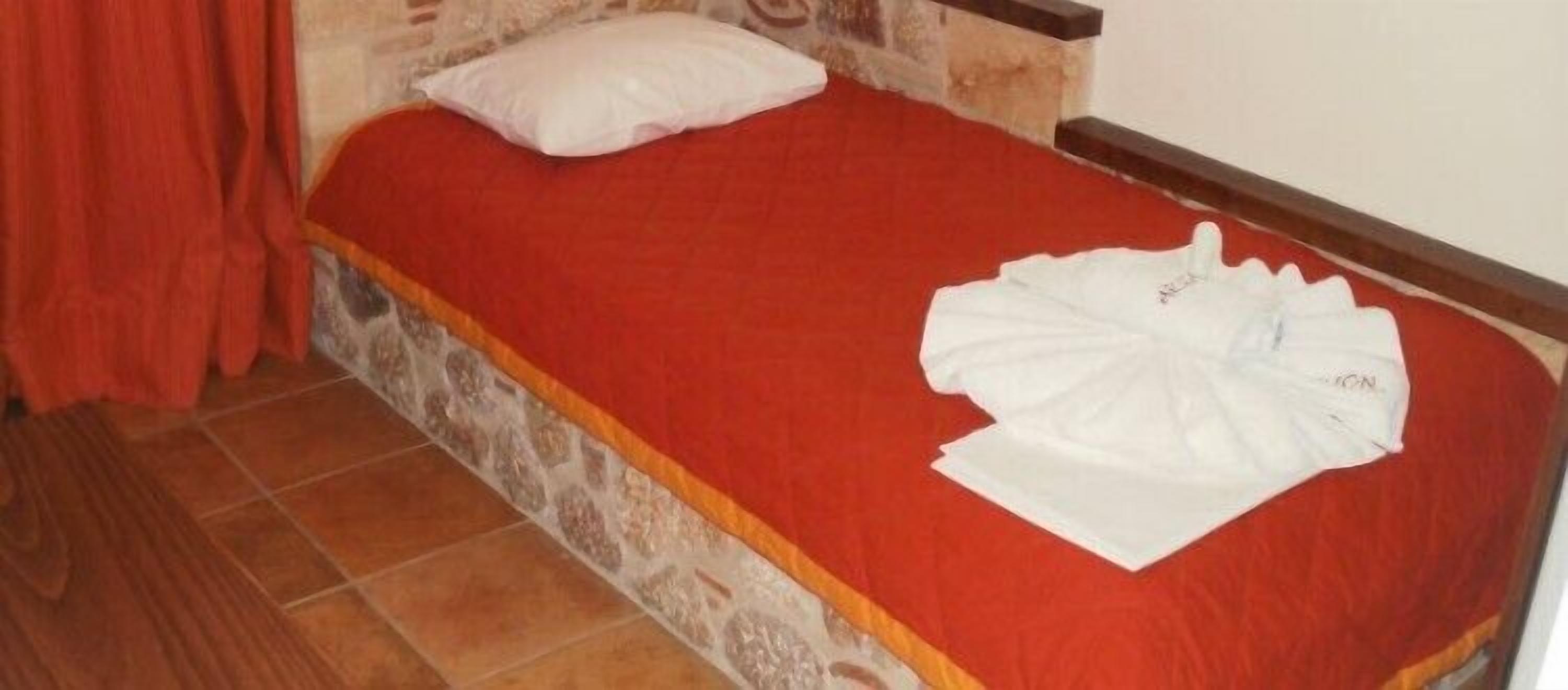 A single bed with a red bedspread and a white pillow.