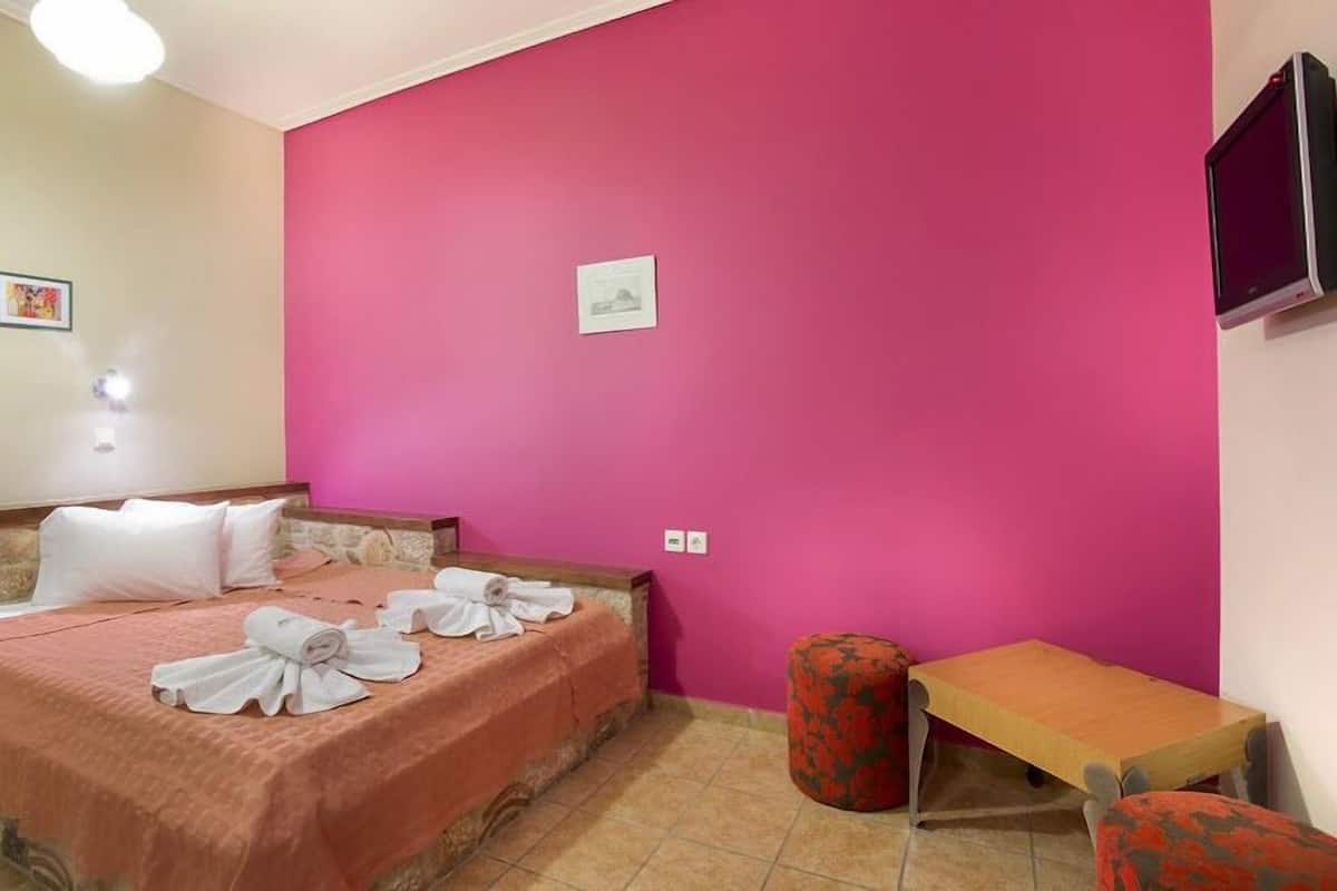 Quarto de hotel com cama, uma mesinha e televisão presa na parede.