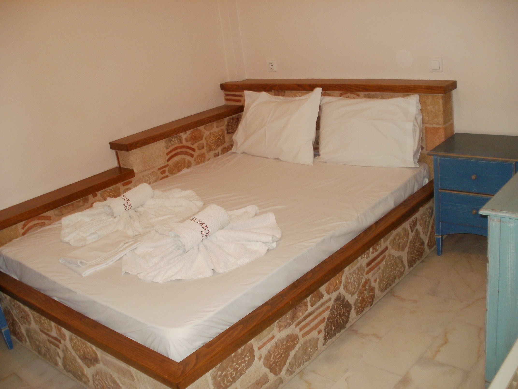 Una cama individual con cabecera de diseño de piedra, una mesita de noche de madera con cajones y una pared lisa.