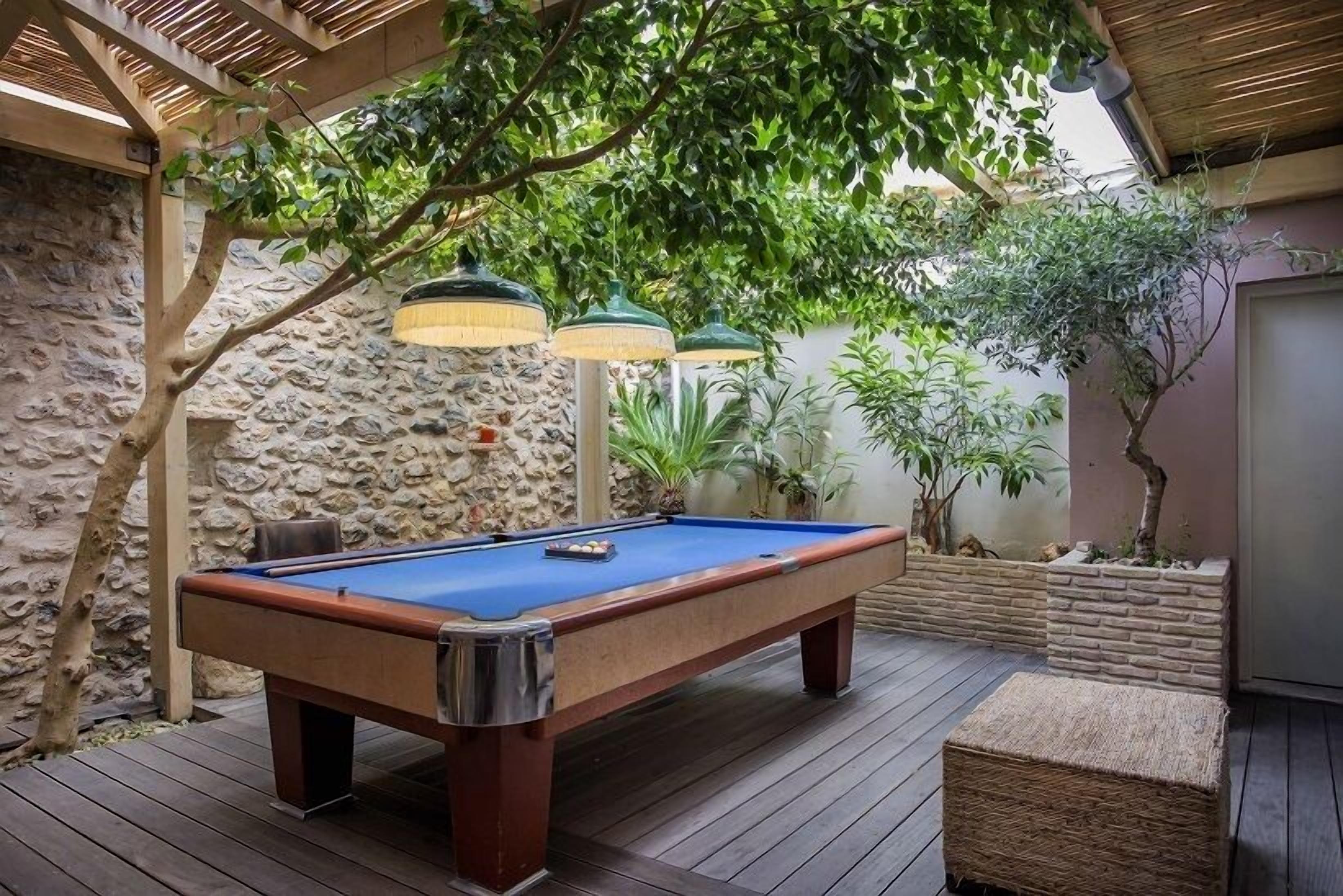 Una mesa de billar en un espacio exterior cubierto con paredes de piedra y vigas de madera.
