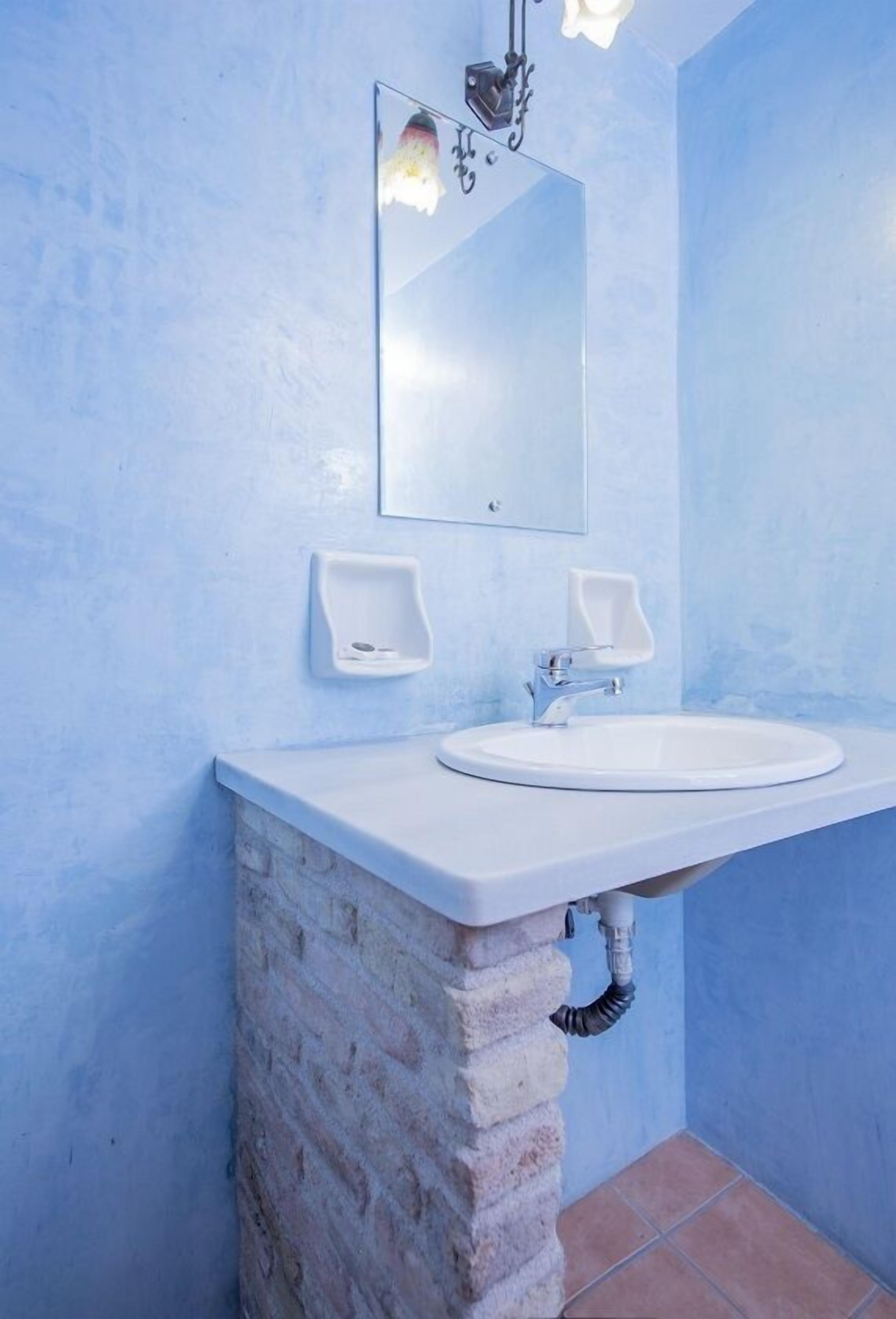 A bathroom with a white sink, two soap dispensers, a mirror, and a light fixture.