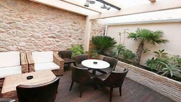 A covered patio with a stone wall, a round table, and several chairs.