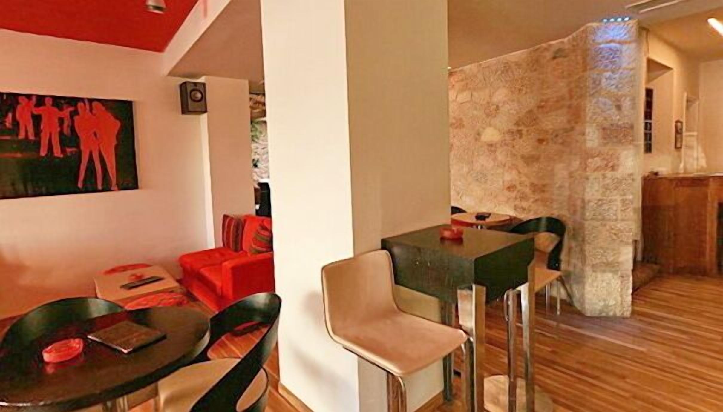 Un salon moderne avec un canapé rouge, un coin repas comprenant une table et des chaises, et un mur d’accent en pierre.