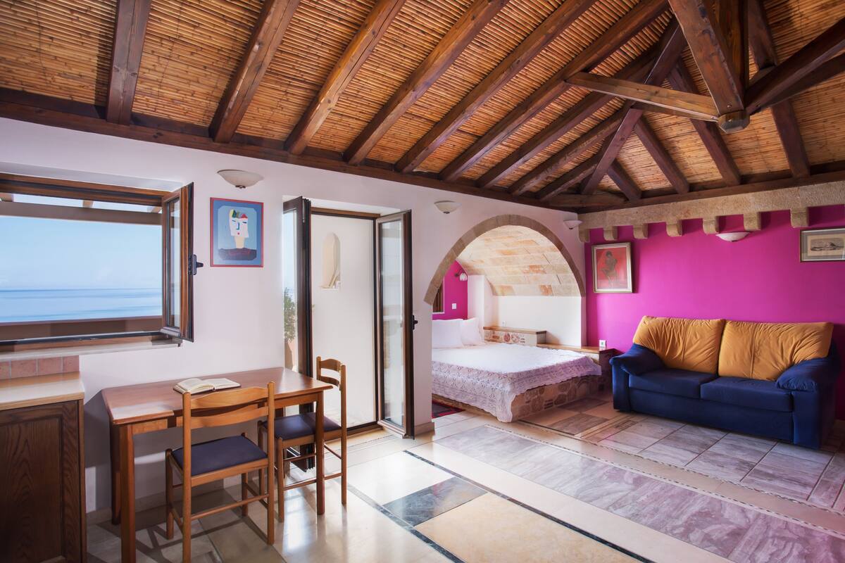 Um quarto com teto de madeira, uma cama, um sofá e uma mesa com cadeiras.