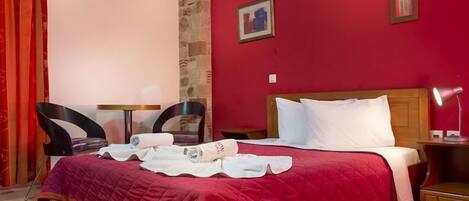 A hotel room with a red wall, a wooden bed, a nightstand, a lamp, and a chair.