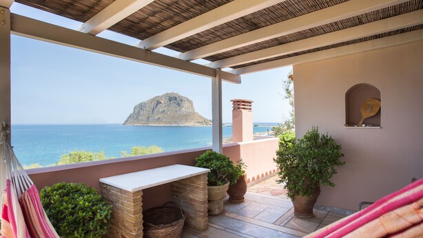 A balcony with a view of the sea and a mountain, featuring a table, chairs, and potted plants. - Aktaion Hotel (Monemvasia)