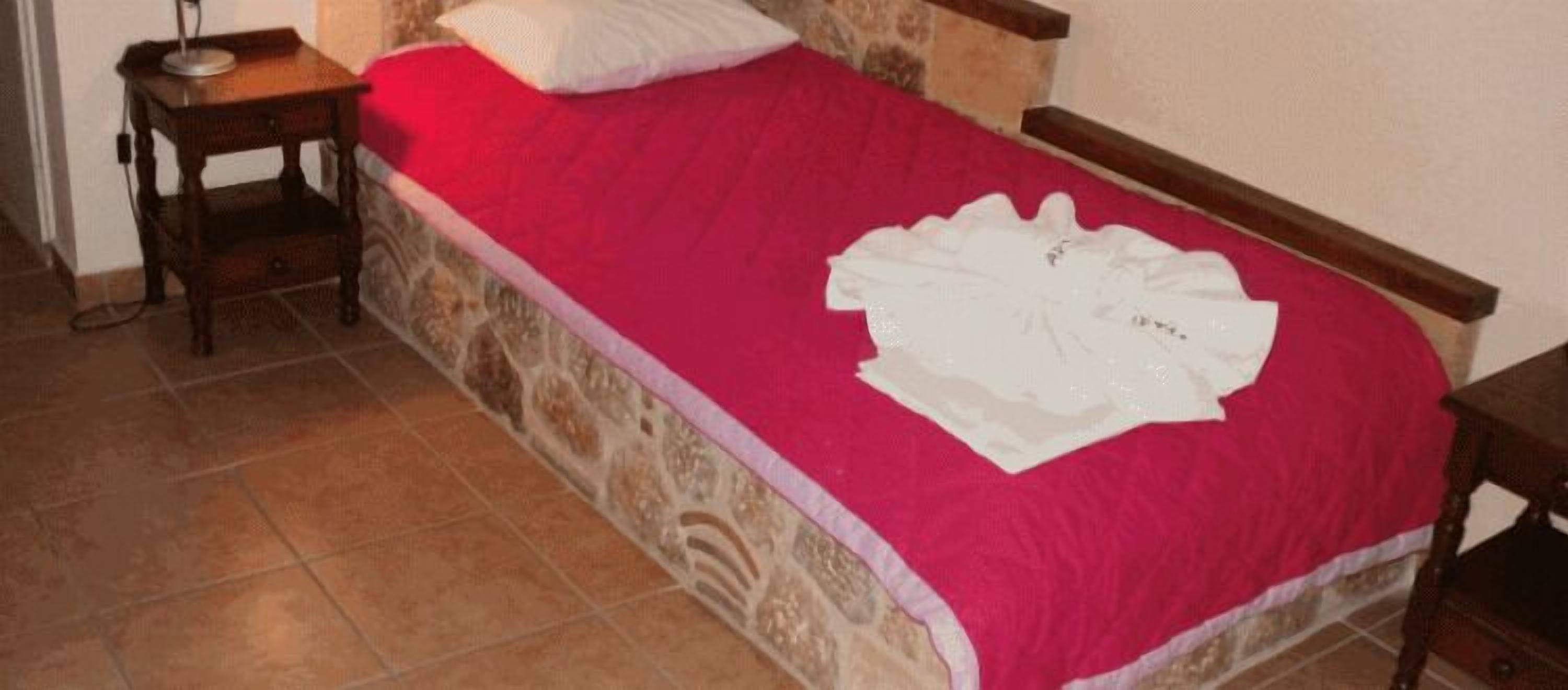 A single bed with a red bedspread and a white decorative pillow.