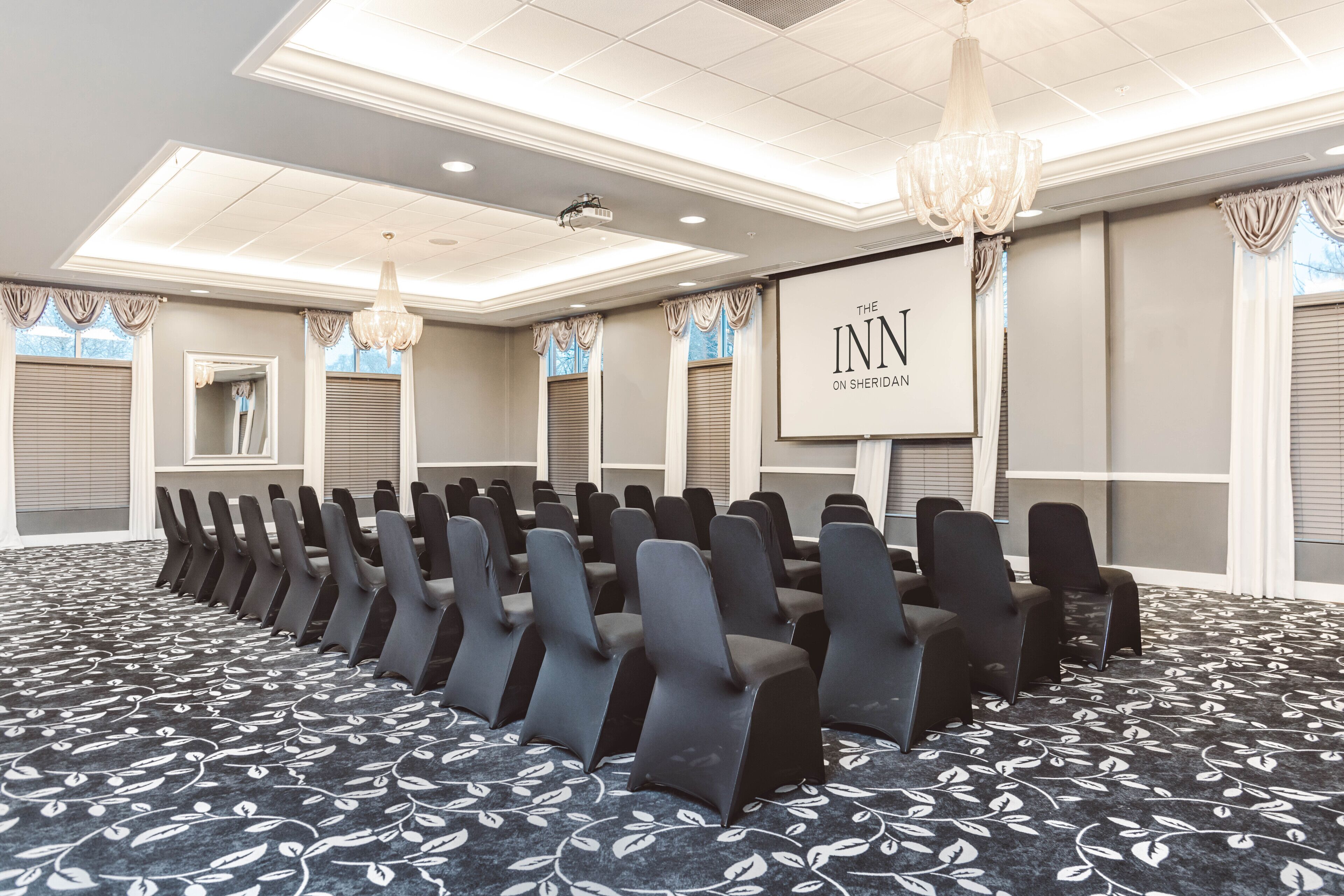 A conference room with rows of chairs, a projector screen, and a carpet with a leaf pattern.