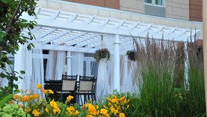 A covered outdoor seating area with a white pergola, a table with chairs, and hanging flower baskets.