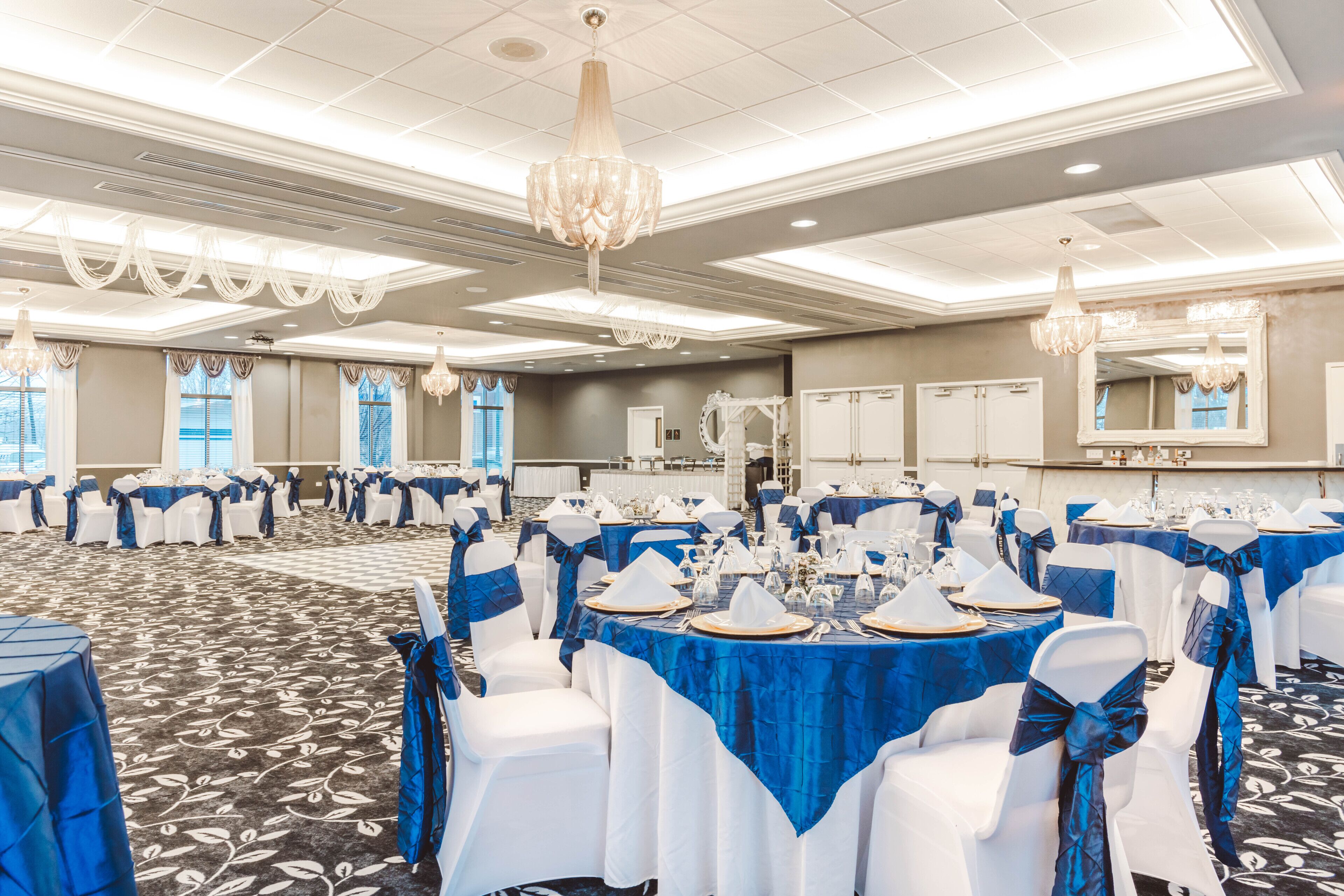 A banquet hall with round tables set for events, featuring white chairs with blue sashes and tables covered with blue tablecloths.