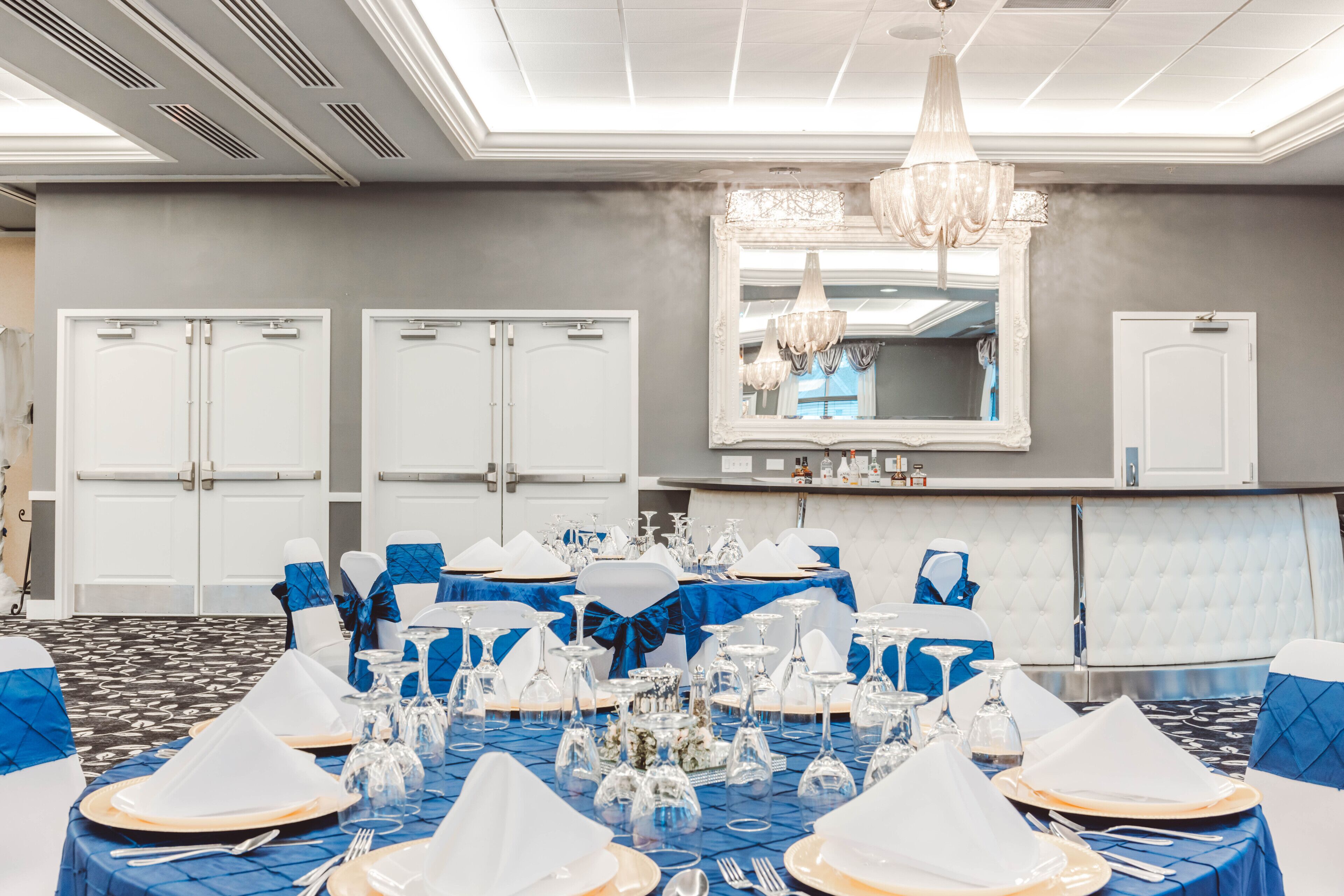 A banquet hall with round tables set for a formal event, featuring blue tablecloths, white napkins, and gold cutlery.