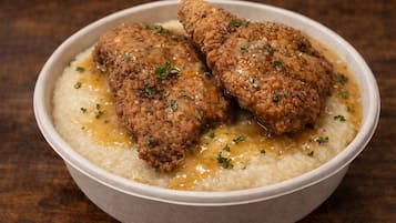 Un tazón de comida con pollo empanizado y una base cremosa, posiblemente un gratinado o sopa.