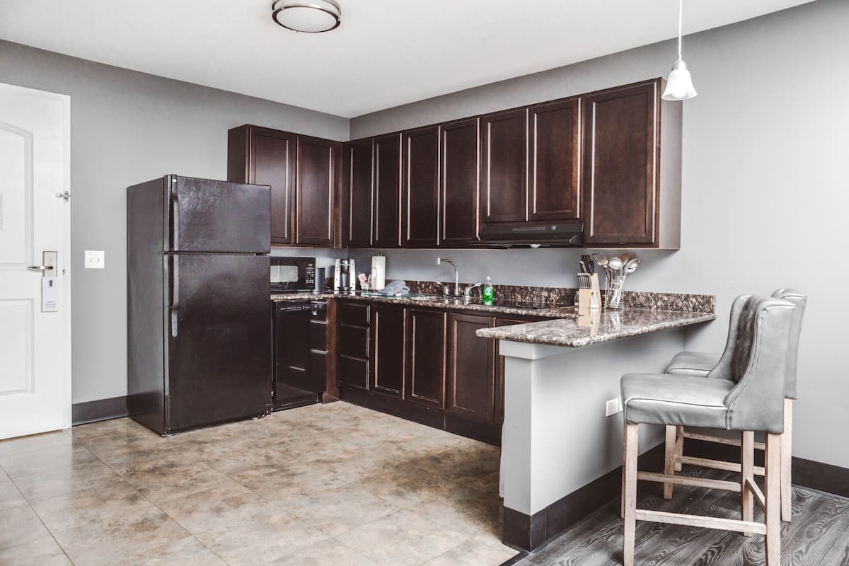 A modern kitchen with dark wood cabinets, a stainless steel refrigerator, a microwave, and a granite countertop.