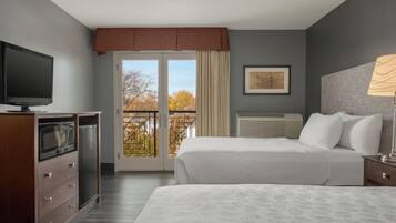 A hotel room with a bed, a TV, a desk, and a window with a view of trees.