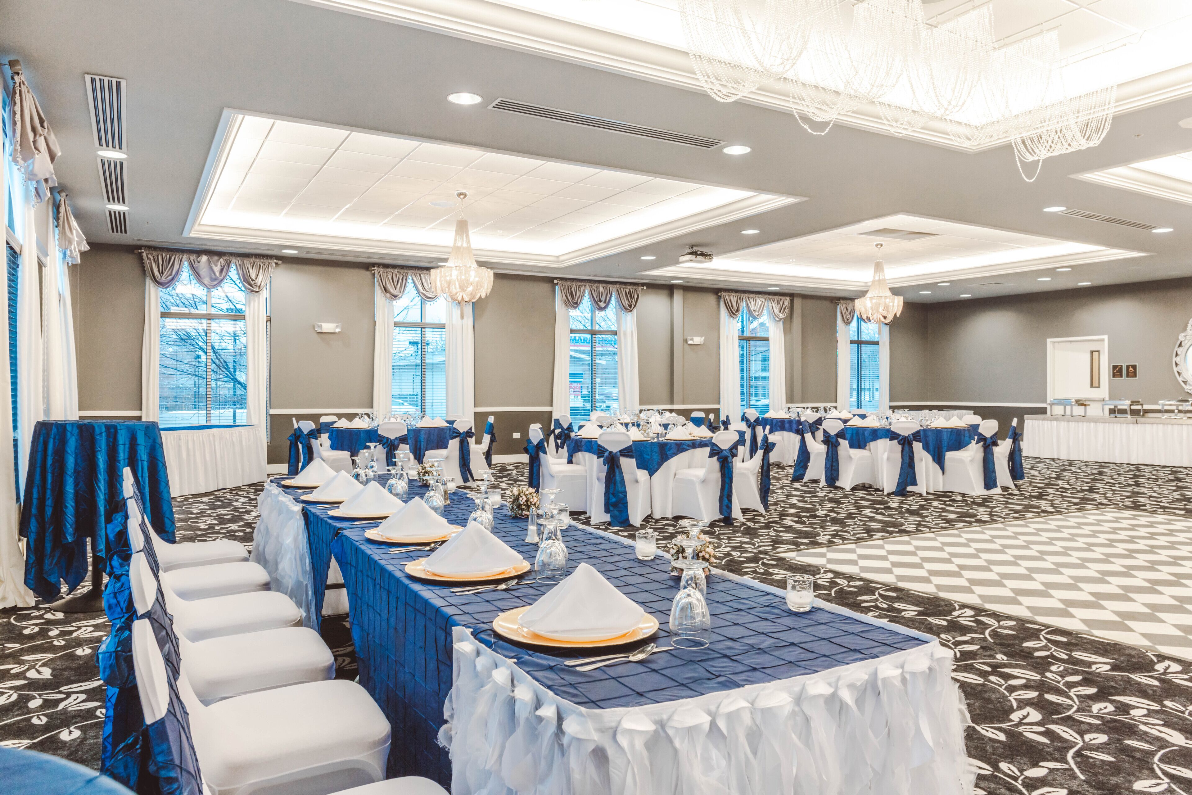 A banquet hall with tables set for events, featuring a checkered floor and large windows.
