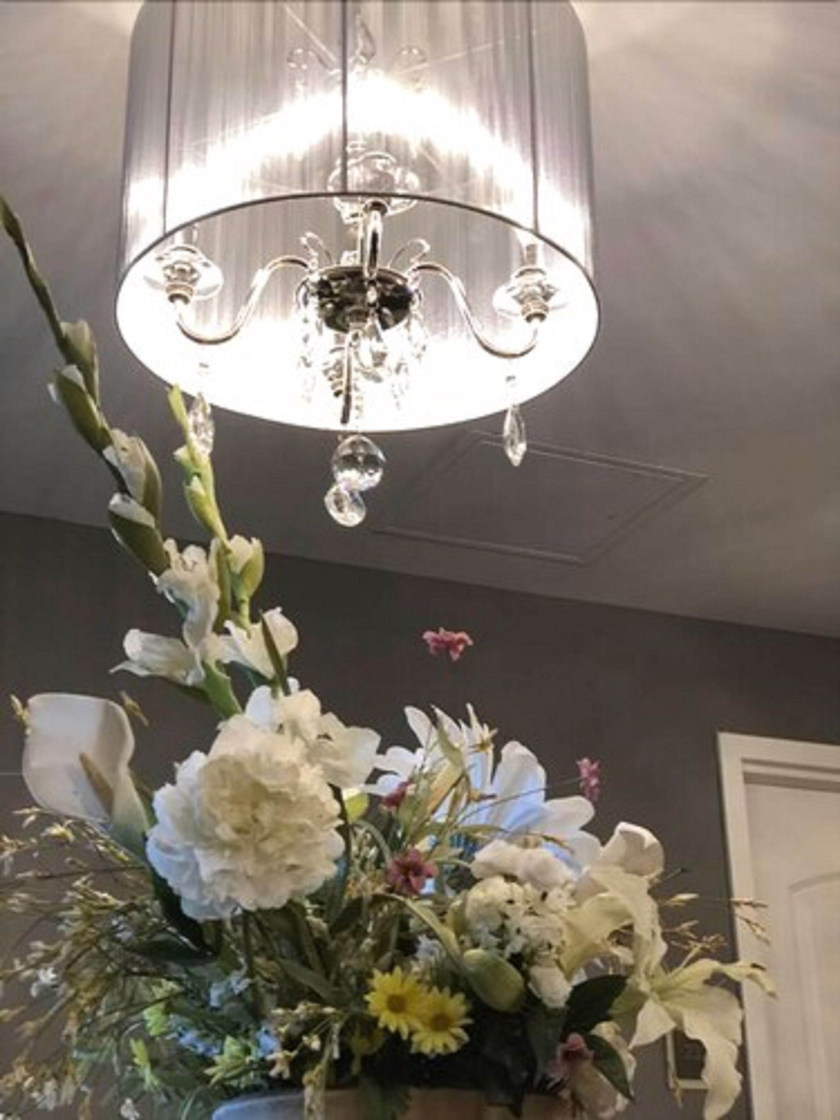 Un candelabro de diseño de cristal, un arreglo floral con flores blancas y amarillas, y una pared de color oscuro.