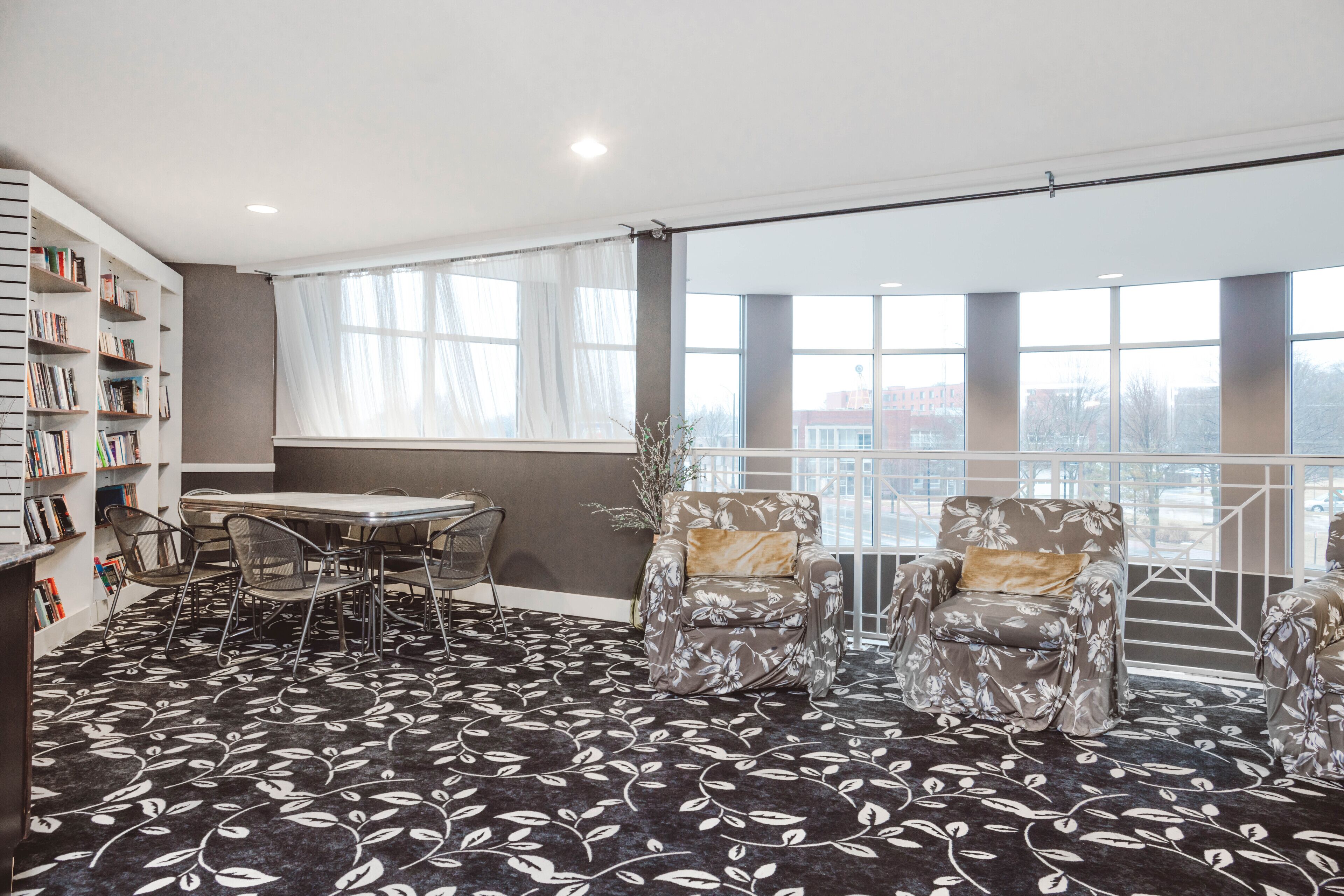 Una habitación amplia con un gran ventanal, una mesa, sillas y una estantería.