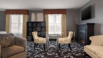 Een hotelkamer met een ronde glazen tafel, twee stoelen, een bank, een open haard en een boekenkast.