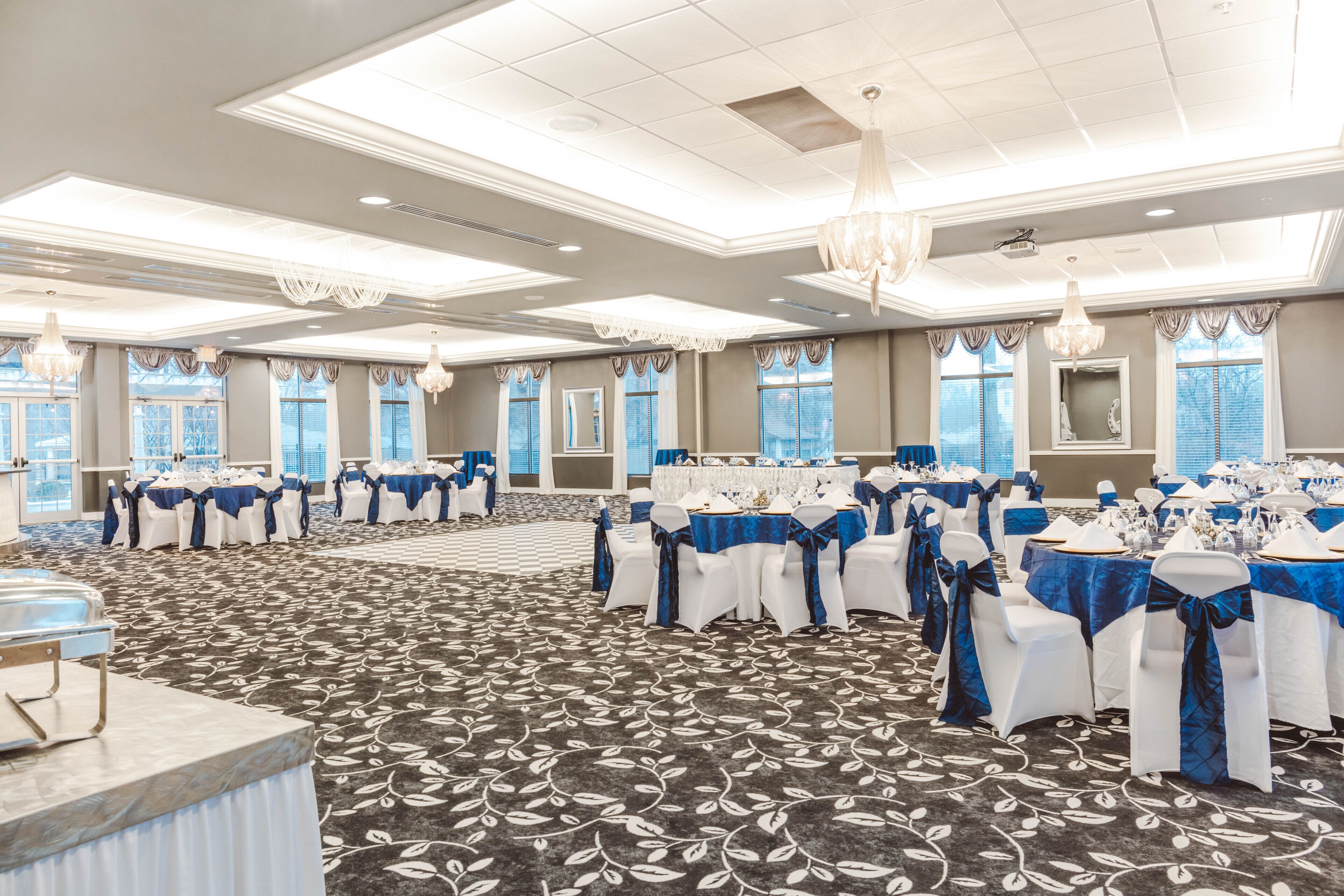 A banquet hall with tables set for a formal event, featuring a carpeted floor and large windows.