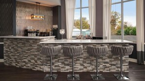 A modern kitchen with a bar area, featuring a stone backsplash, bar stools, and a large window with curtains.