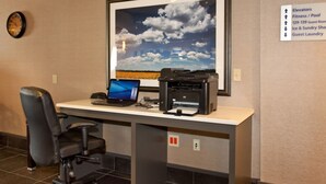 Mostrador de recepción con laptop, impresora y silla, una fotografía enmarco de un paisaje, y un cartel que enumera los servicios del hotel.