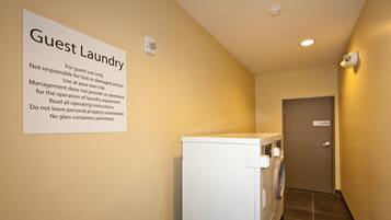 A guest laundry area with a sign detailing usage rules, a washing machine, and a door at the end of the hallway.