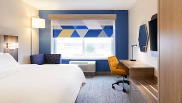 Quarto de hotel com uma cama grande, uma escrivaninha, uma cadeira, janela com vista e televisão na parede.