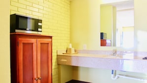 Ein Badezimmer mit Holzschrank, Mikrowelle, Waschbecken und Spiegel.