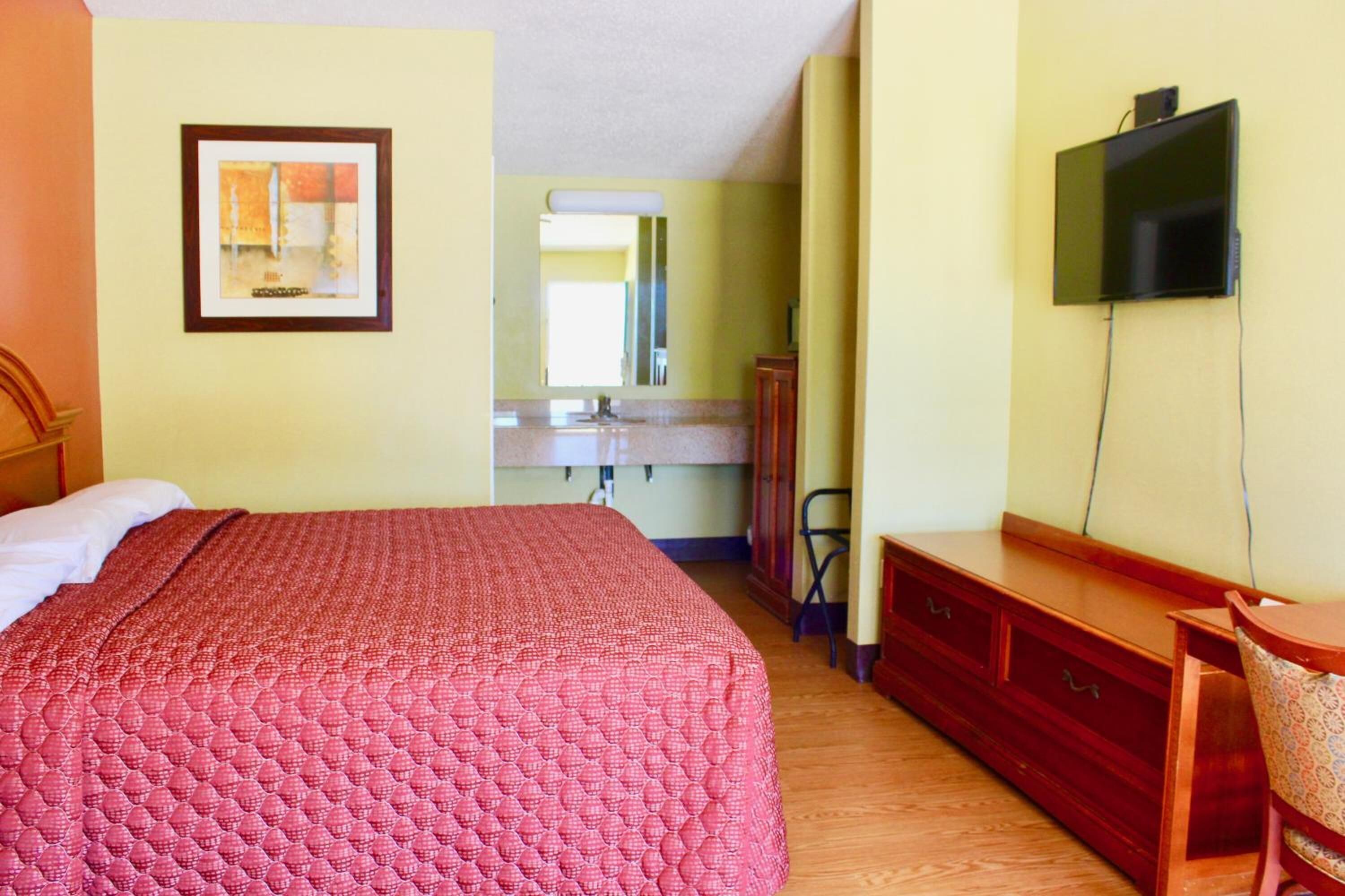 Una camera da letto con un letto, una cassettiera, una televisione e uno specchio.