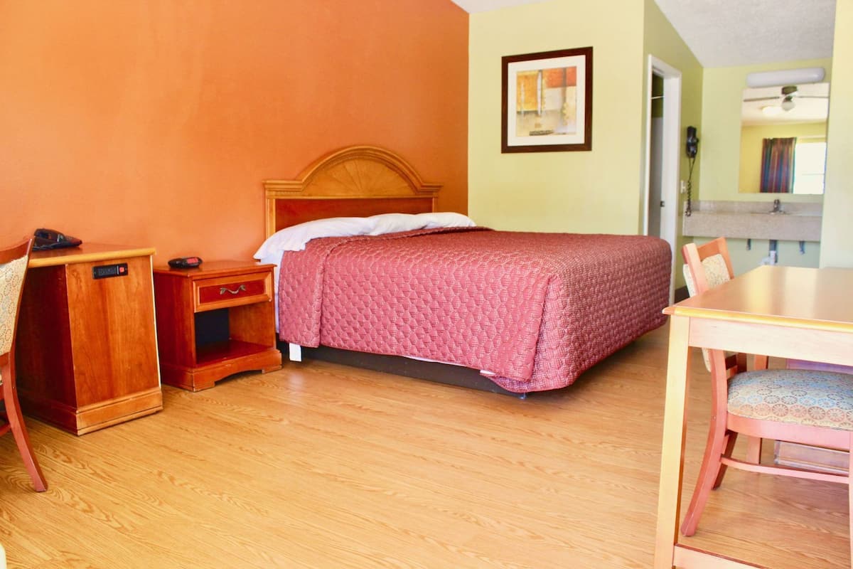 Quarto com cama de madeira, mesa de cabeceira, escrivaninha e cadeira.