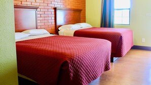 Ein Hotelzimmer mit zwei Betten, einer Ziegelwand, einem Fenster mit Vorhängen und einem Holzboden.
