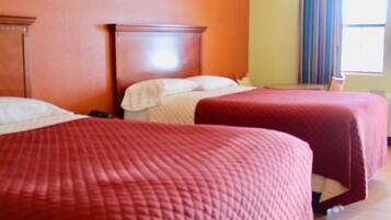 Quarto de hotel com duas camas, uma cabeceira de madeira, uma janela com cortinas e uma mesinha.