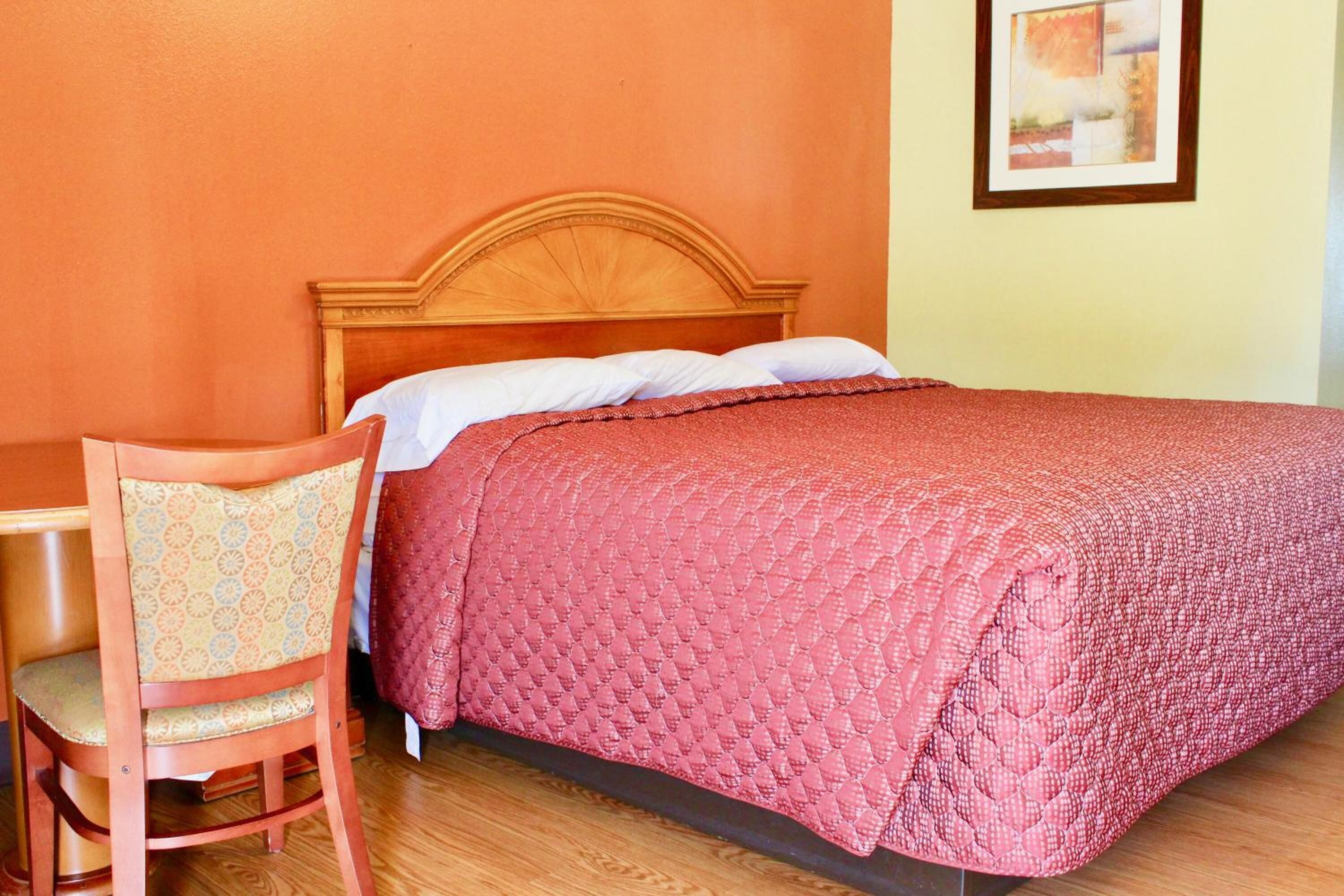 Uma cama bem arrumada com cabeceira de madeira, um edredom vermelho e uma cadeira estofada próxima.