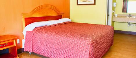 Habitación de hotel con cama de madera, mesita de noche, un cuadro en la pared y un baño visible a través de una puerta abierta.