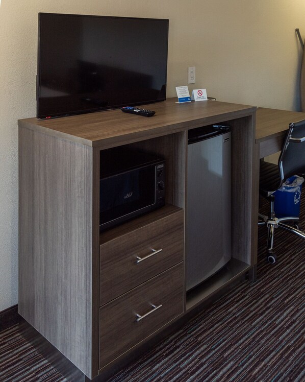 A hotel room with a flat-screen TV, a mini-fridge, a microwave, and a small cabinet with drawers. - Rodeway Inn Near University-Gateway to Yosemite (Merced)