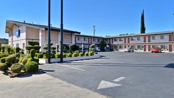 Un motel con estacionamiento, un edificio con letrero y arbustos cuidadosamente recortados.
