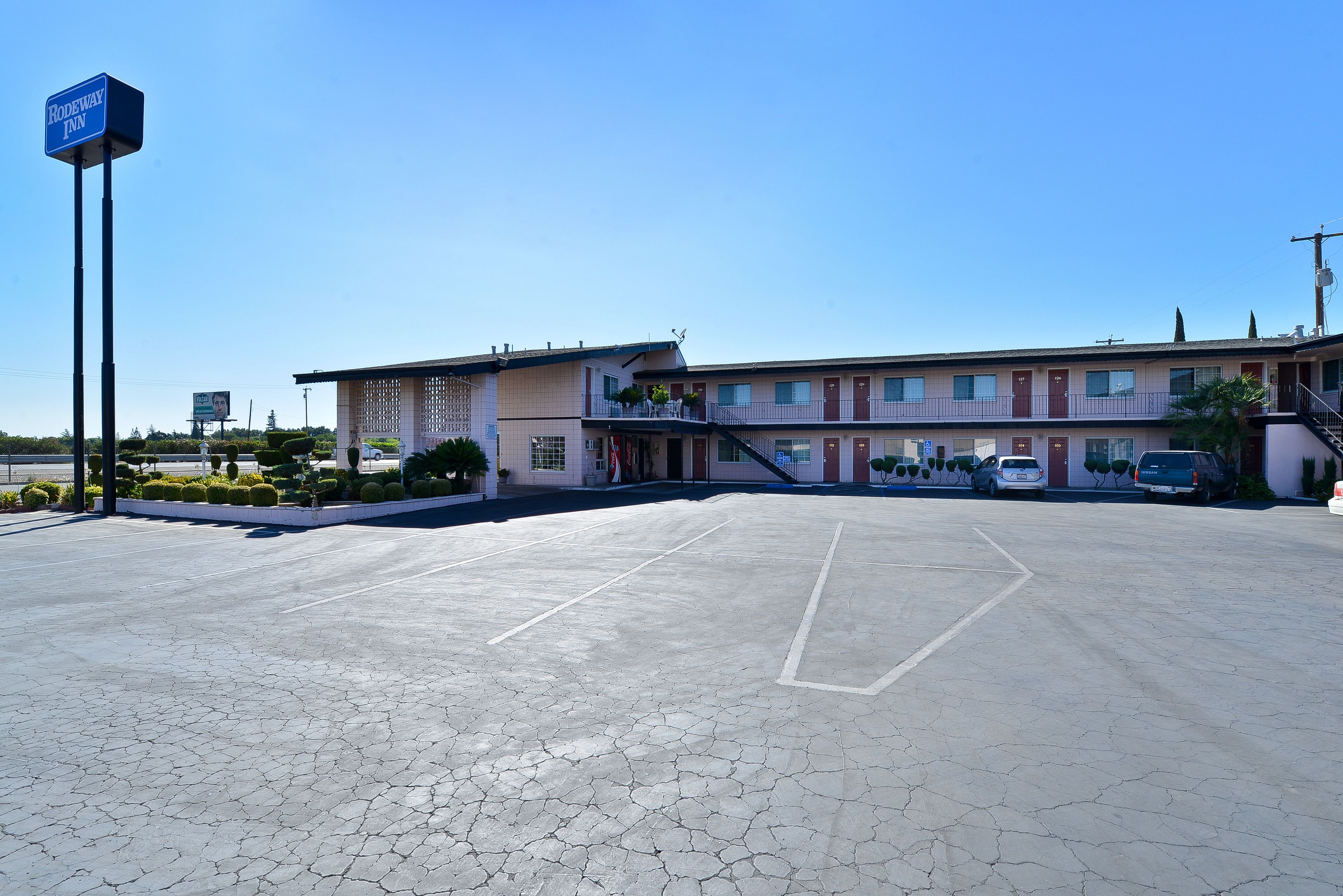Un motel con aparcamiento, un cartel y un edificio con múltiples puertas y ventanas.