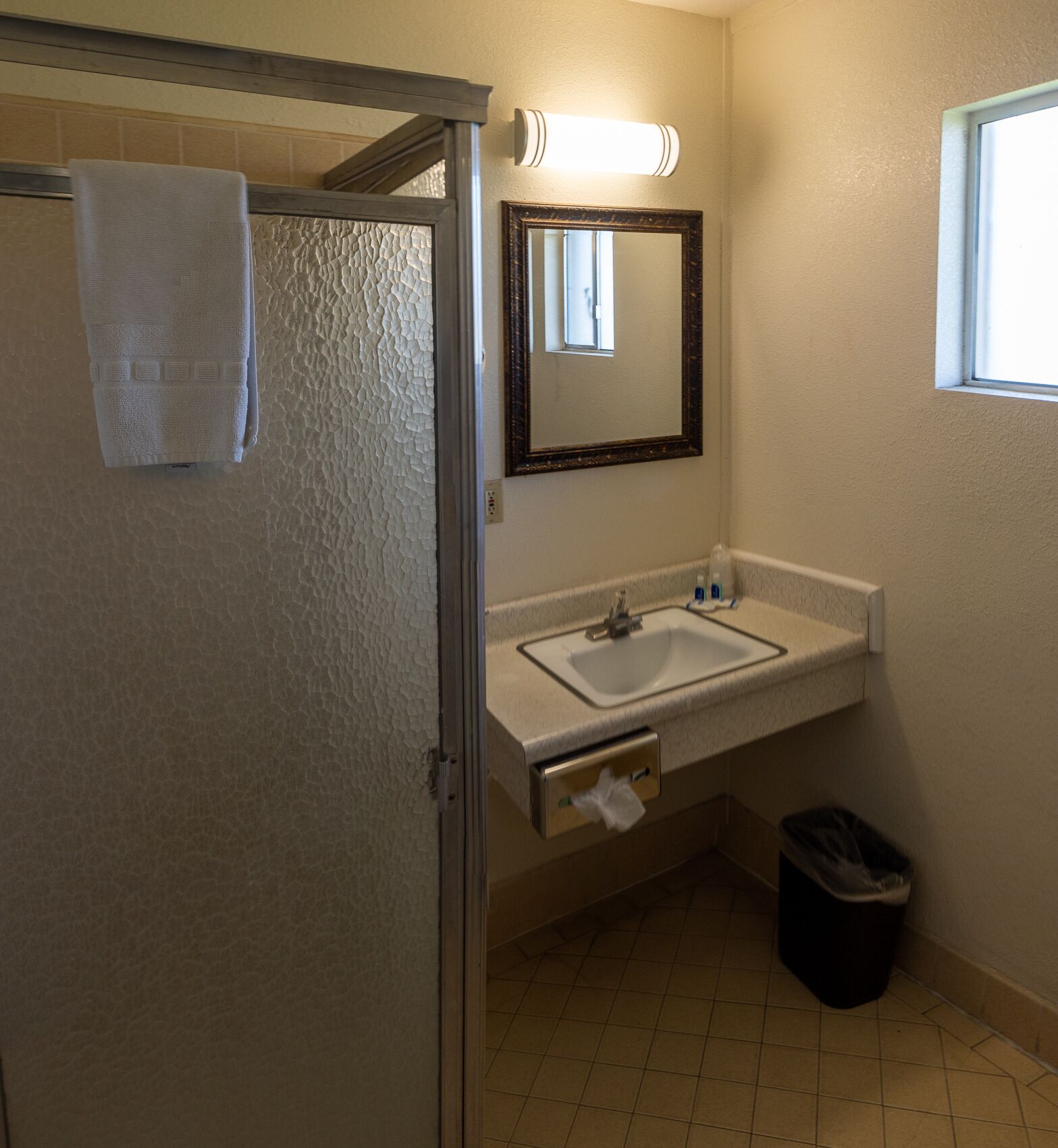 A bathroom with a white sink, a mirror, a towel rack, and a trash bin.