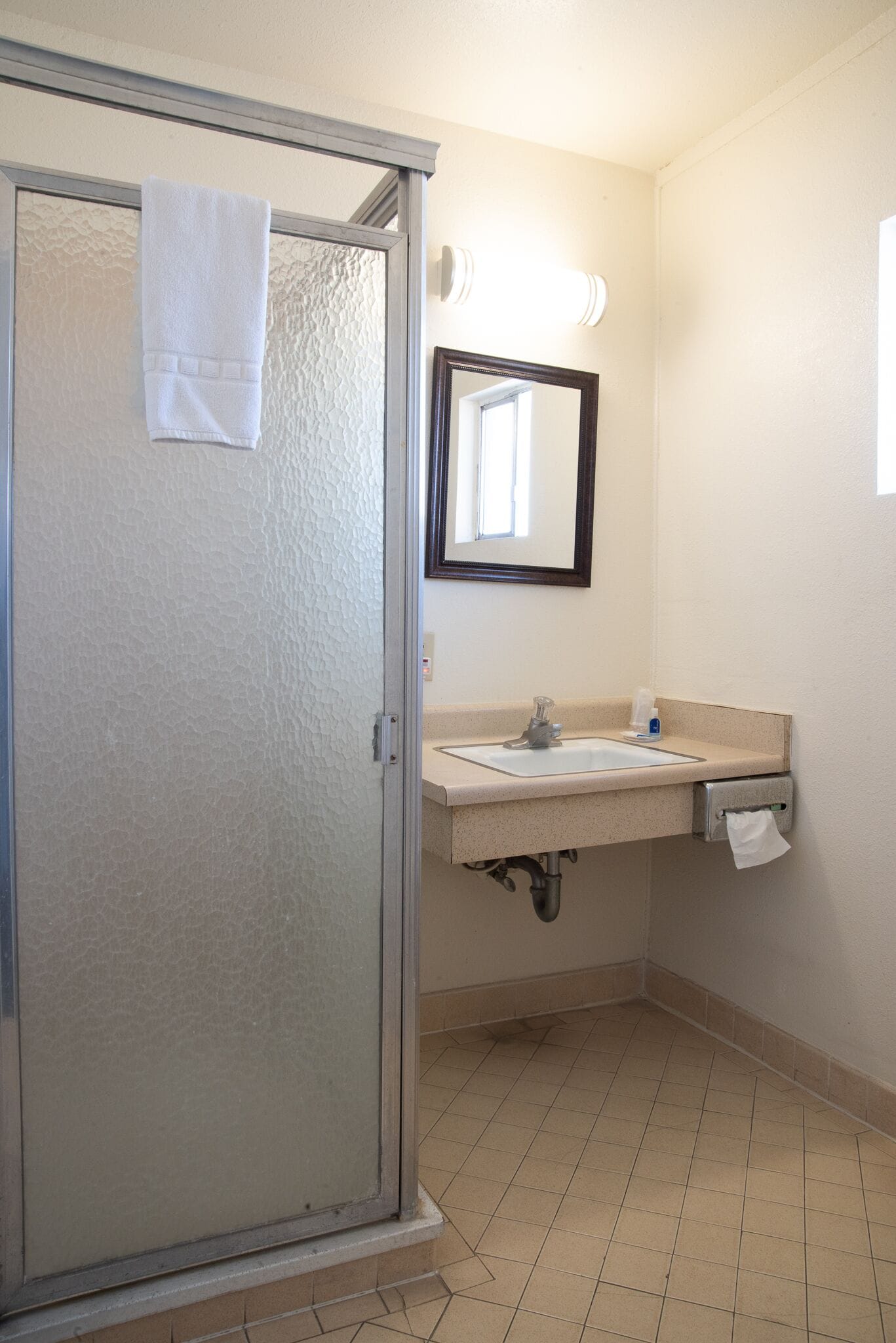 A bathroom with a glass shower door, a sink with a mirror, and a towel hanging on the door.