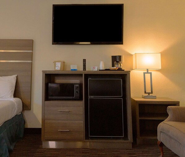 A hotel room with a bed, a TV mounted on the wall, a microwave, a mini fridge, a lamp, and a small table with a coffee maker. - Rodeway Inn Near University-Gateway to Yosemite (Merced)