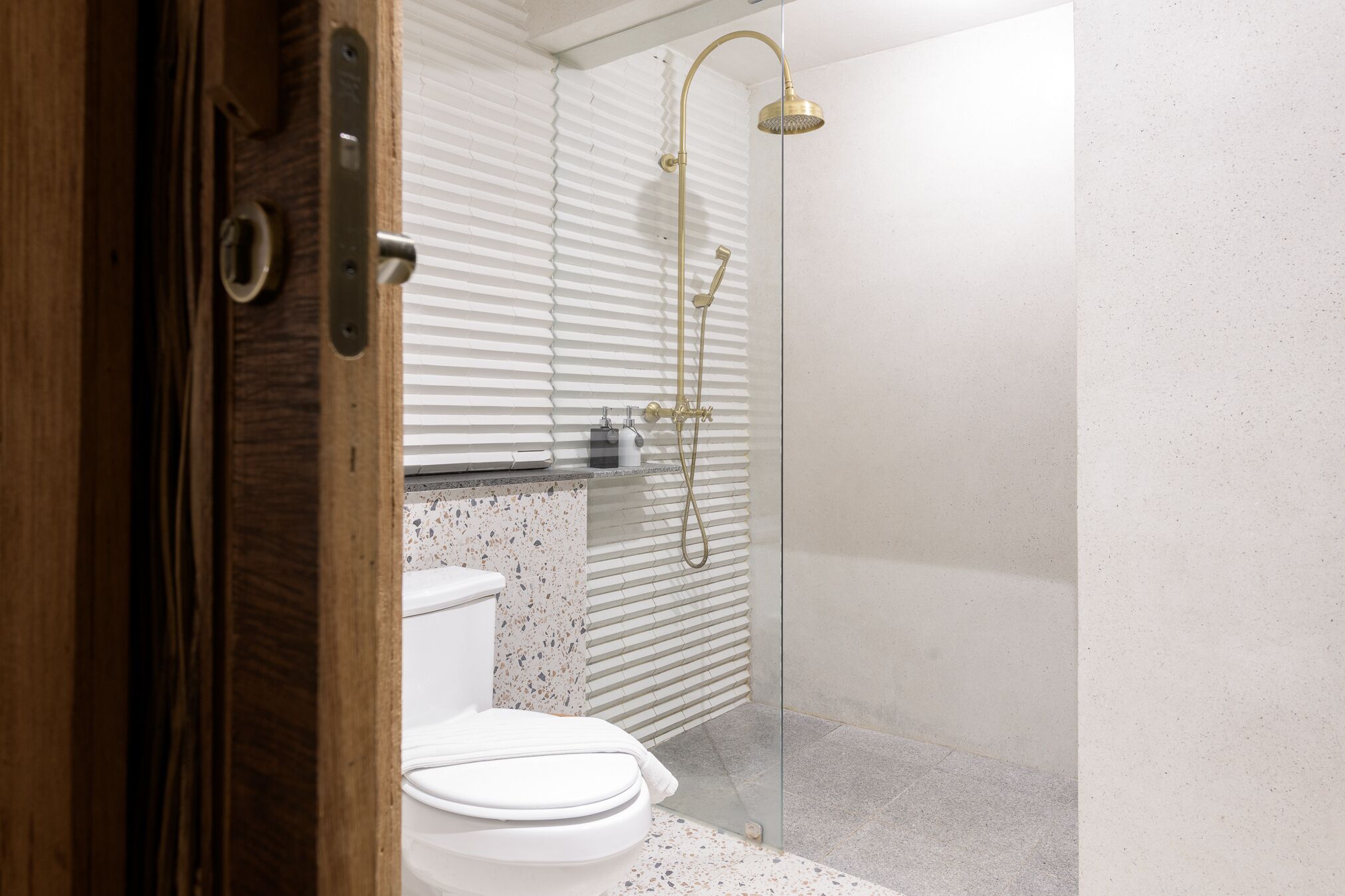 Un baño moderno con cabina de ducha de vidrio, inodoro y puerta de madera.