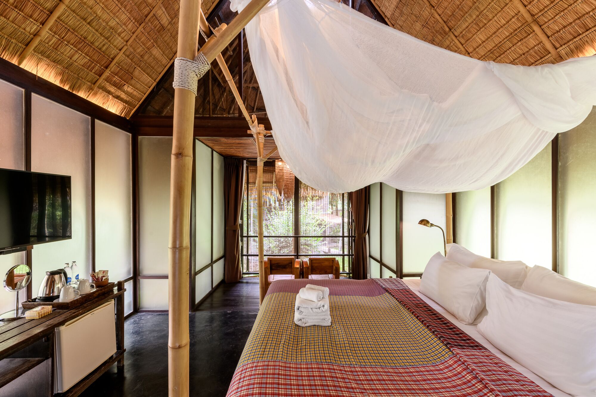 Una habitación con una cama, televisión, escritorio y ventana con vistas a zonas verdes.