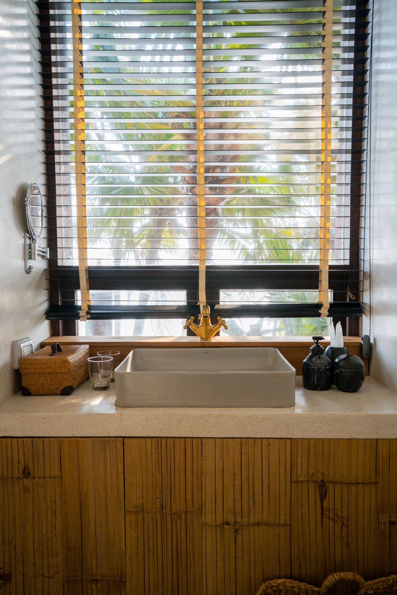A bathroom with a wooden vanity, a white sink, and a window with vertical blinds.