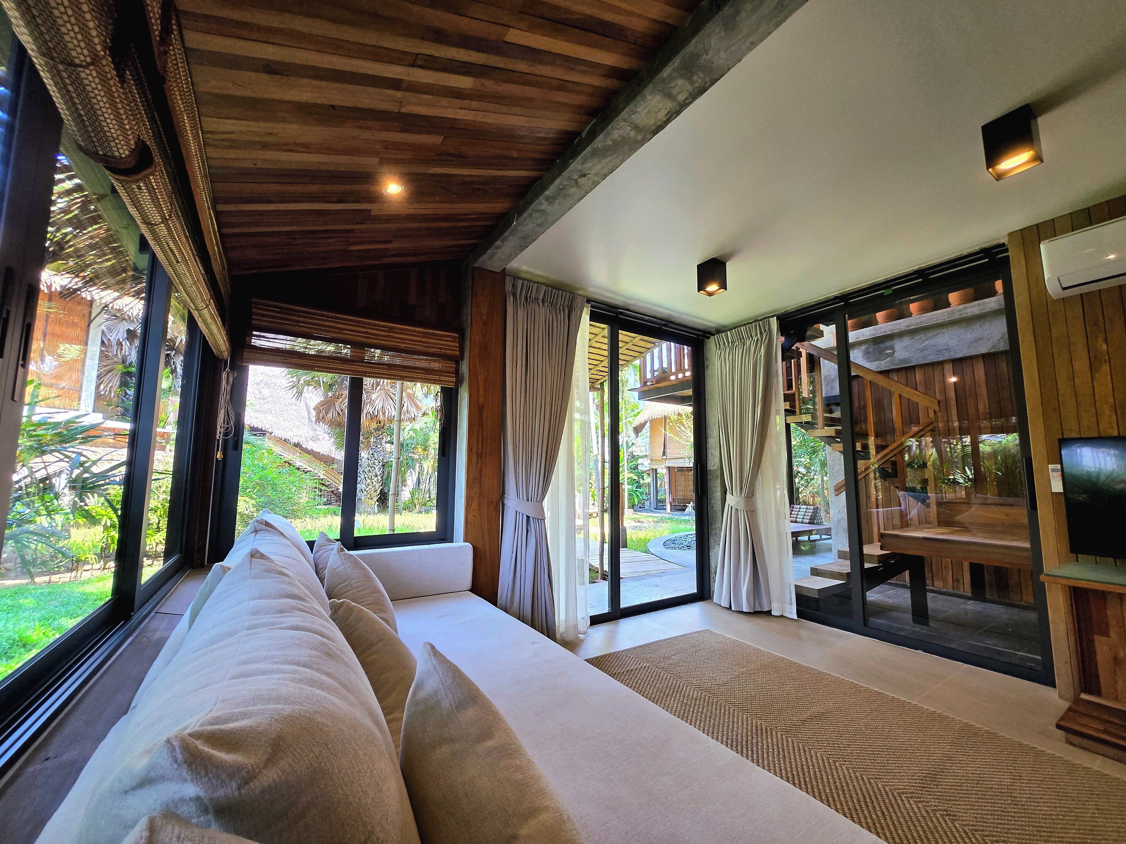 Una habitación con un sofá grande, una televisión y vistas a un jardín a través de amplios ventanales.