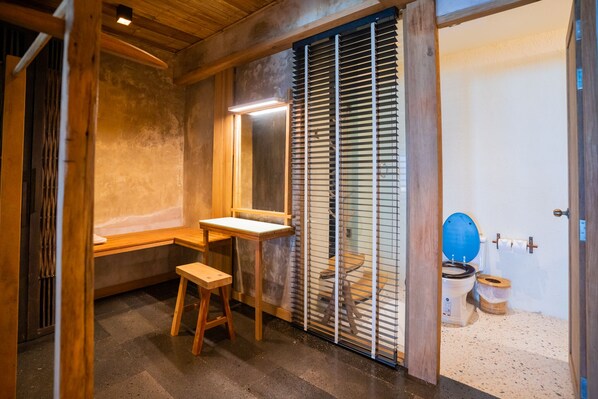 Une salle de bain de style japonais traditionnel, avec un banc en bois, des toilettes dotées d’un abattant bleu et un paravent coulissant de type shoji.
